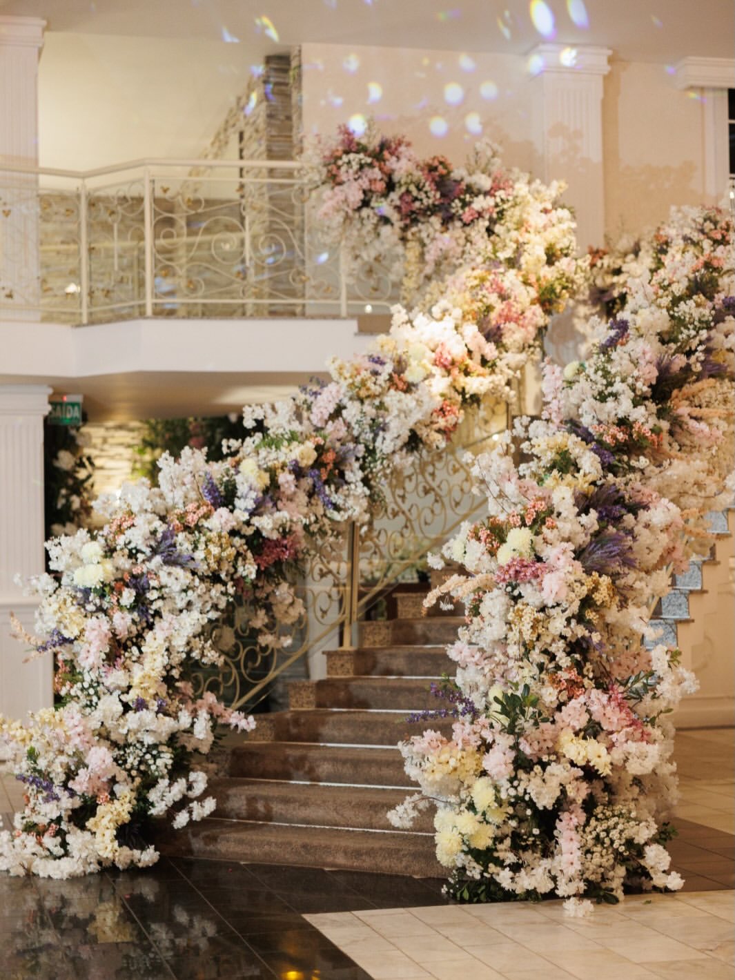 Escadaria tomada por arranjos florais em tons pastel em salão de festas